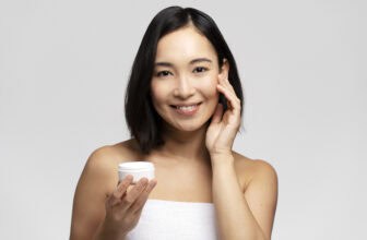 Dazzling young woman applying Mixsoon Antiaging cream on her face. Photo of woman in white towel on studio background. Skin care concept