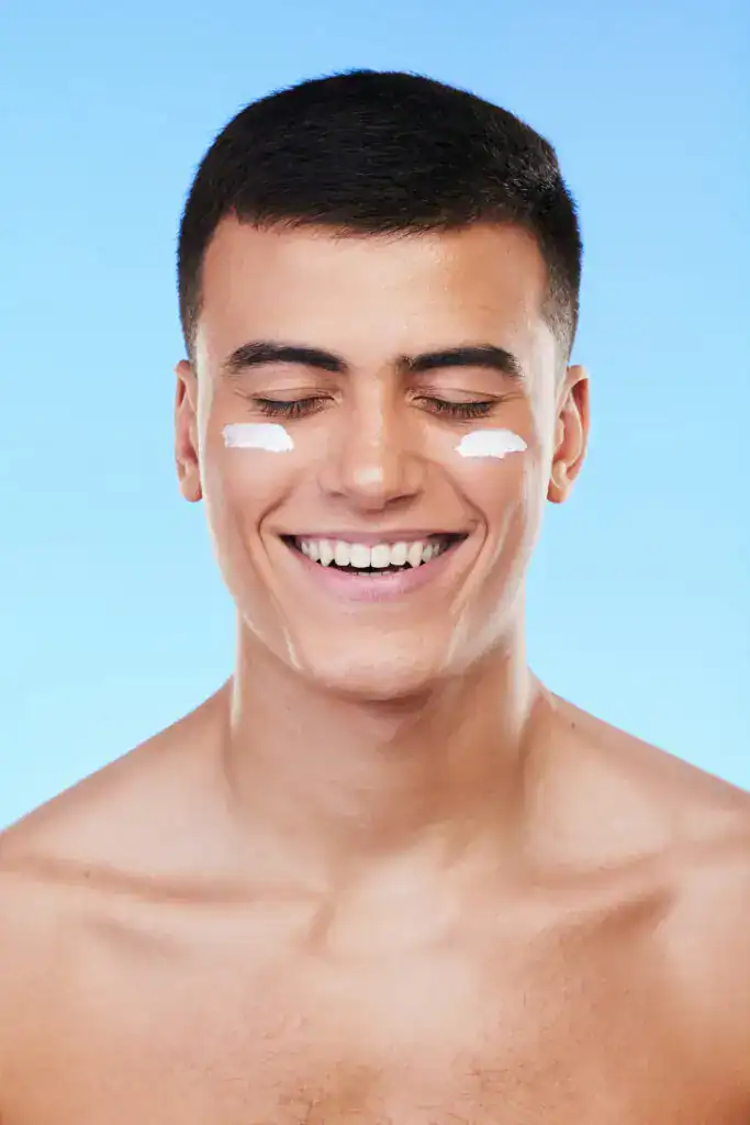 Man, beauty and face with lotion on skin, moisturizer and grooming for hygiene isolated on blue bac.